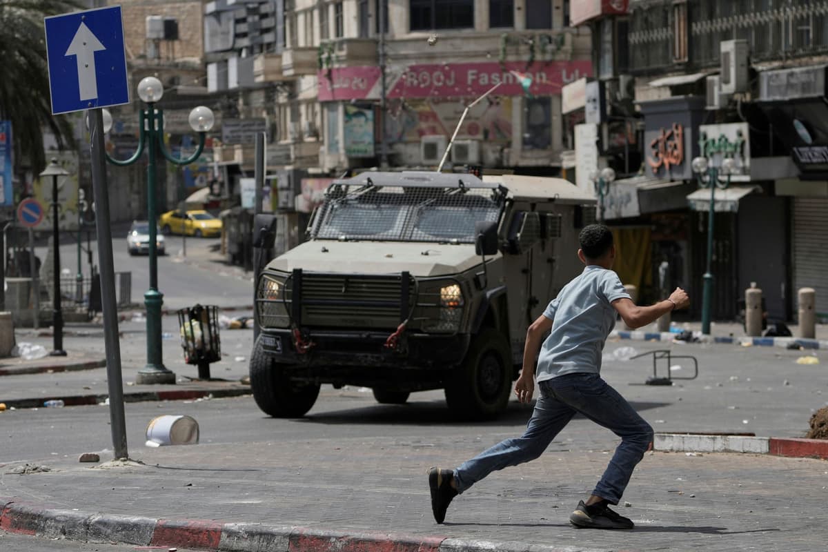 Palestínčan beží pred obrneným vozidlom počas zrážok s izraelskými silami po vojenskom nájazde v meste Nablus na Západnom brehu. Foto: TASR/AP
