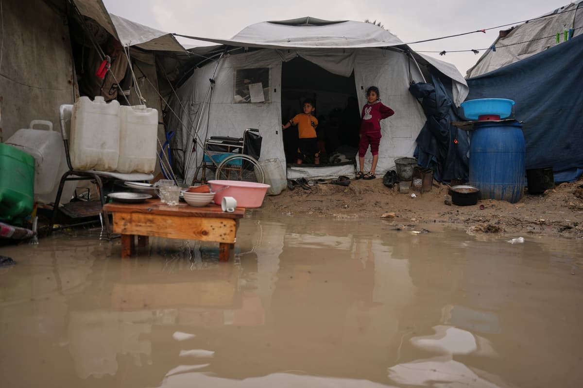 Vysídlené palestínske deti stoja pri vstupe do ich rodinného stanu na zaplavenej ulici po prudkých dažďoch v utečeneckom tábore v meste Dajr al-Balah 12. decembra 2025. Foto: TASR/AP