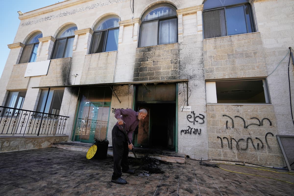 Muž odpratáva trosky, pričom na stene je v hebrejčine napísané: „pomsta, pozdravy zatknutým. Foto: TASR/AP